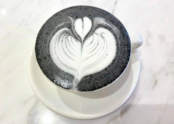 A top-down shot of a black sesame latte, with a heart-shaped design in white foam.